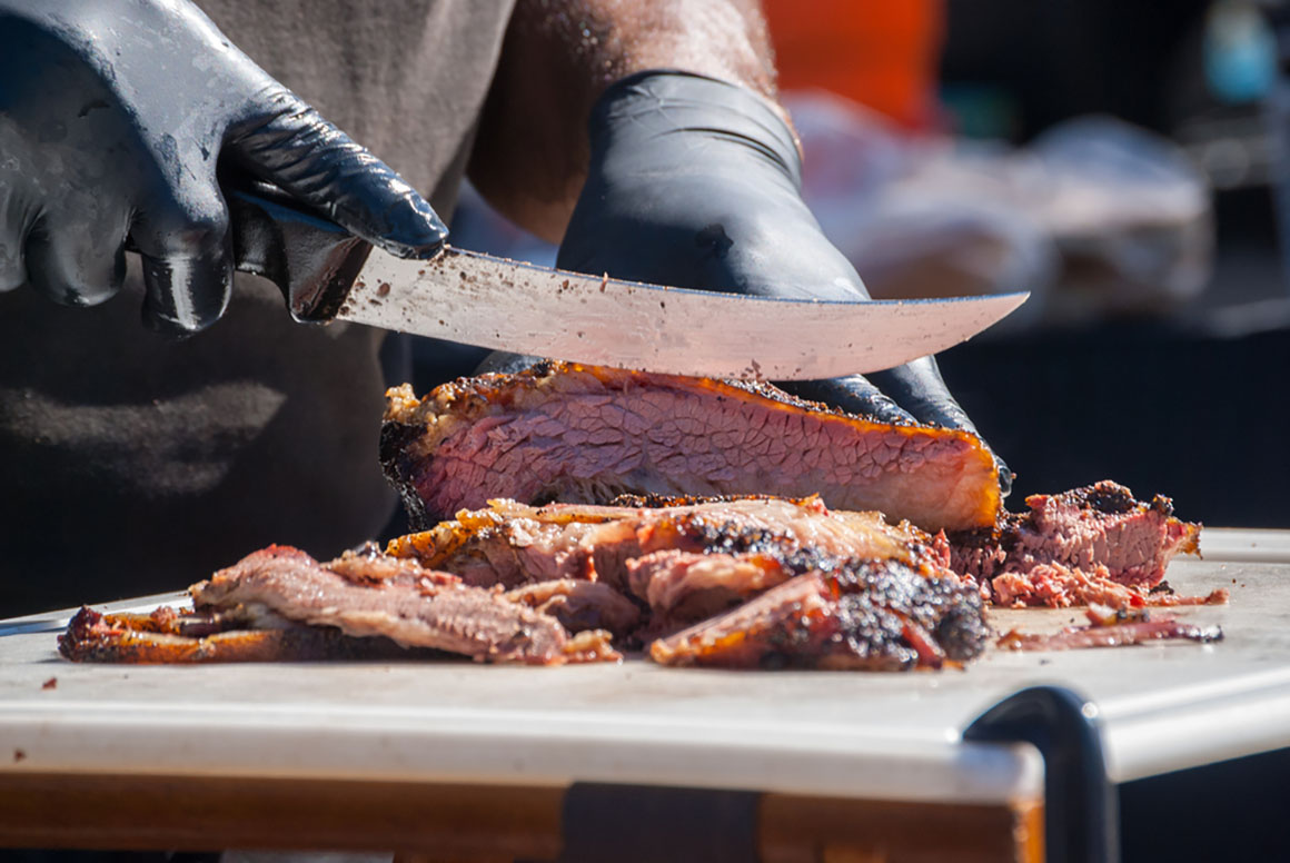 Hands slicing beef fresh out of the smoker.