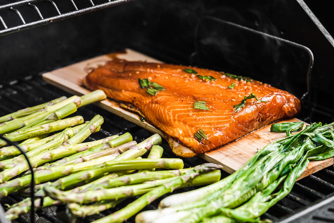 Grilled veggies on a charcoal grill. Asparagus and onions caramelizing. Salmon on a cedar wood plank grilling and smoking.