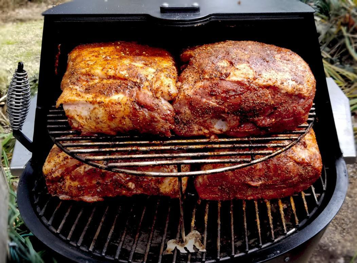 four large slabs of meat cooking on a small grill