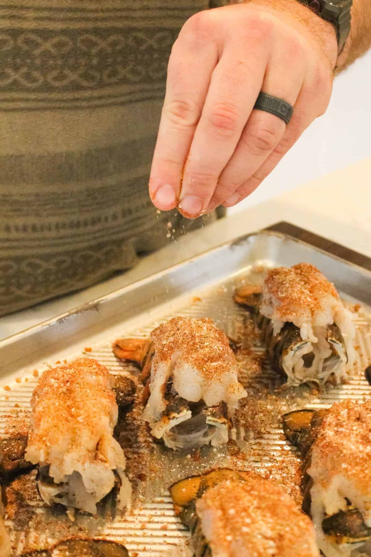 Honey Cajun Smoked Lobster Tails getting sprinkled with seasoning. 