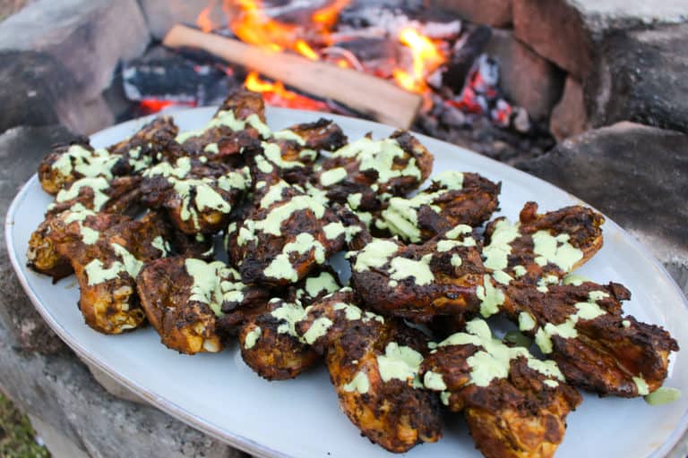 Butterflied Peruvian Chicken Drumsticks with Green Sauce plated by the fire.