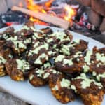 Butterflied Peruvian Chicken Drumsticks with Green Sauce plated by the fire.