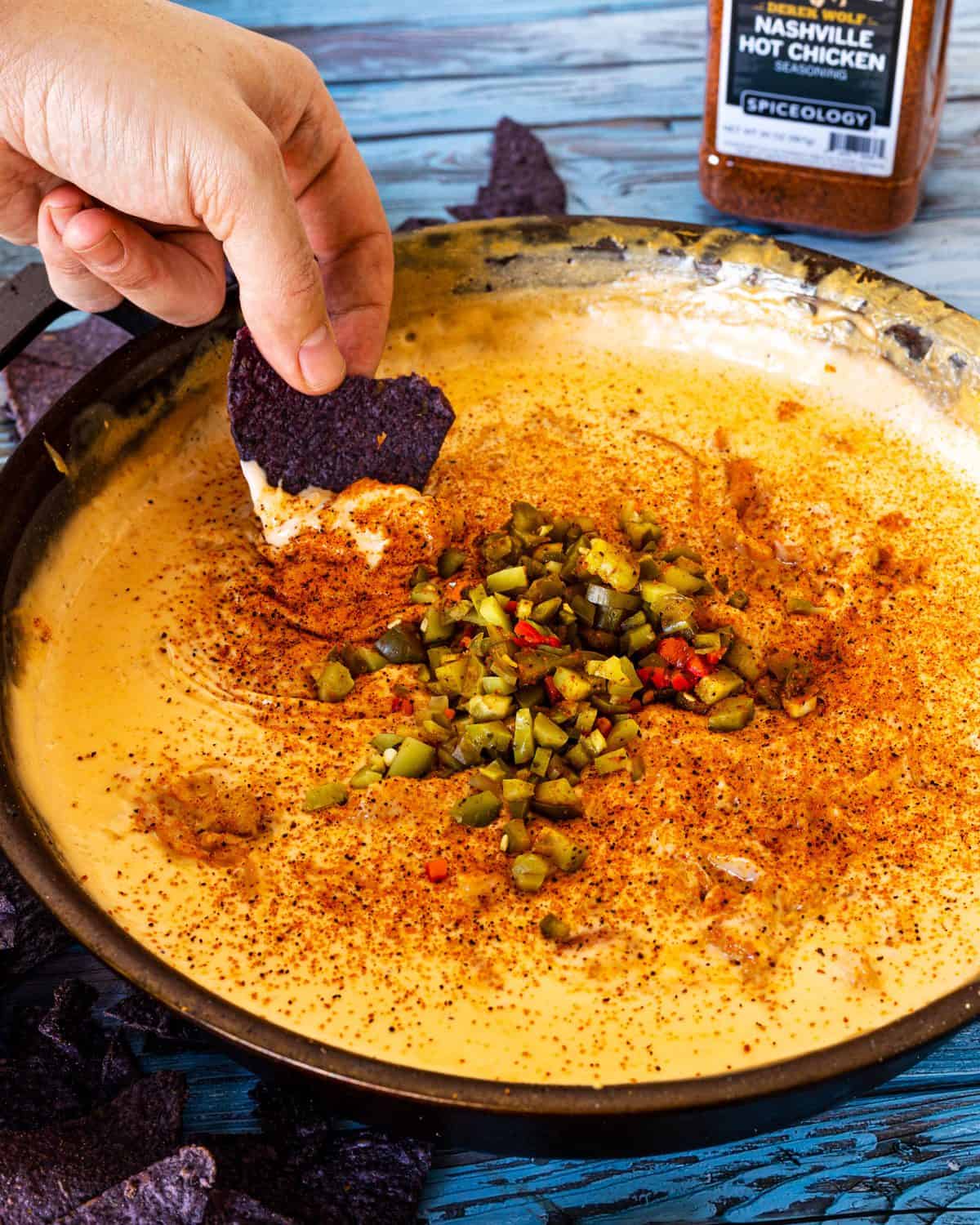 A chip getting dipped into Smoked Nashville Hot Chicken Queso.