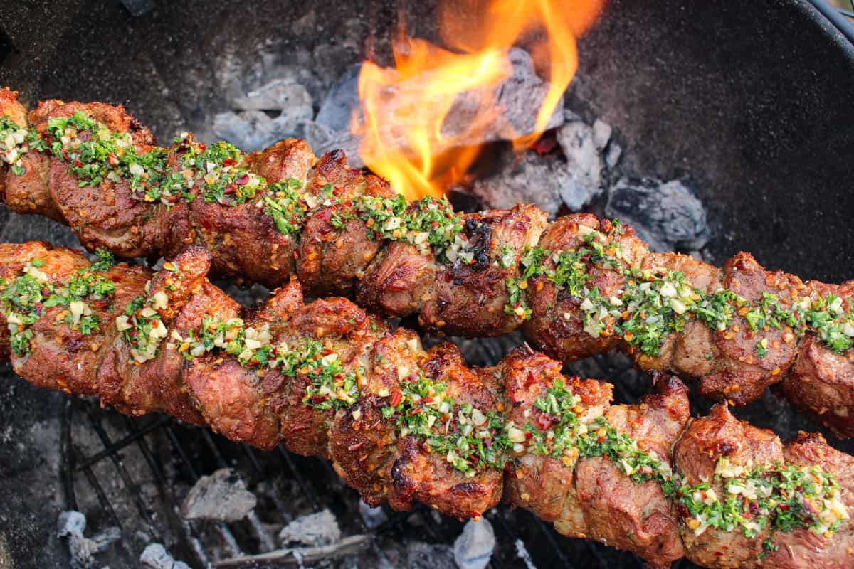 A close up shot the the lamb with chimichurri as it finishes cooking over the coals. 