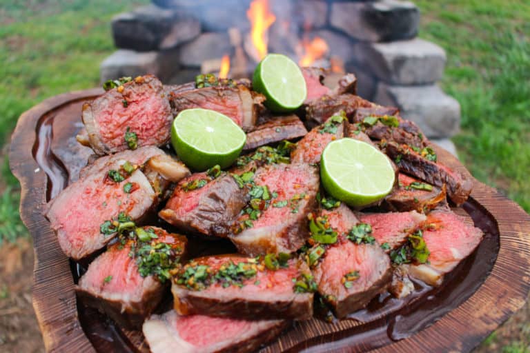 Grilled NY Strips with Garlic Chili Sauce sitting on a cutting board in front of the flames.