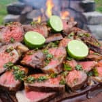 Grilled NY Strips with Garlic Chili Sauce sitting on a cutting board in front of the flames.