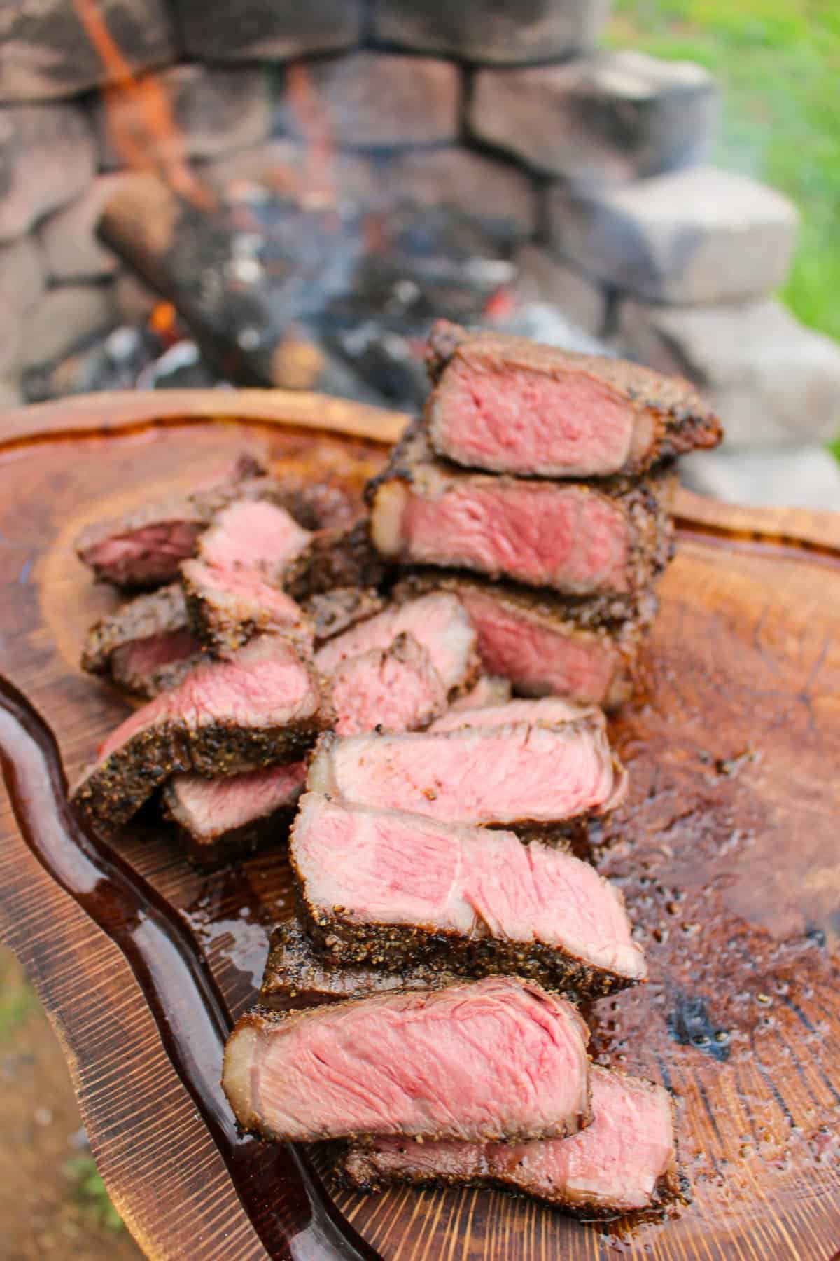 sliced steak on a cutting board next to a fire