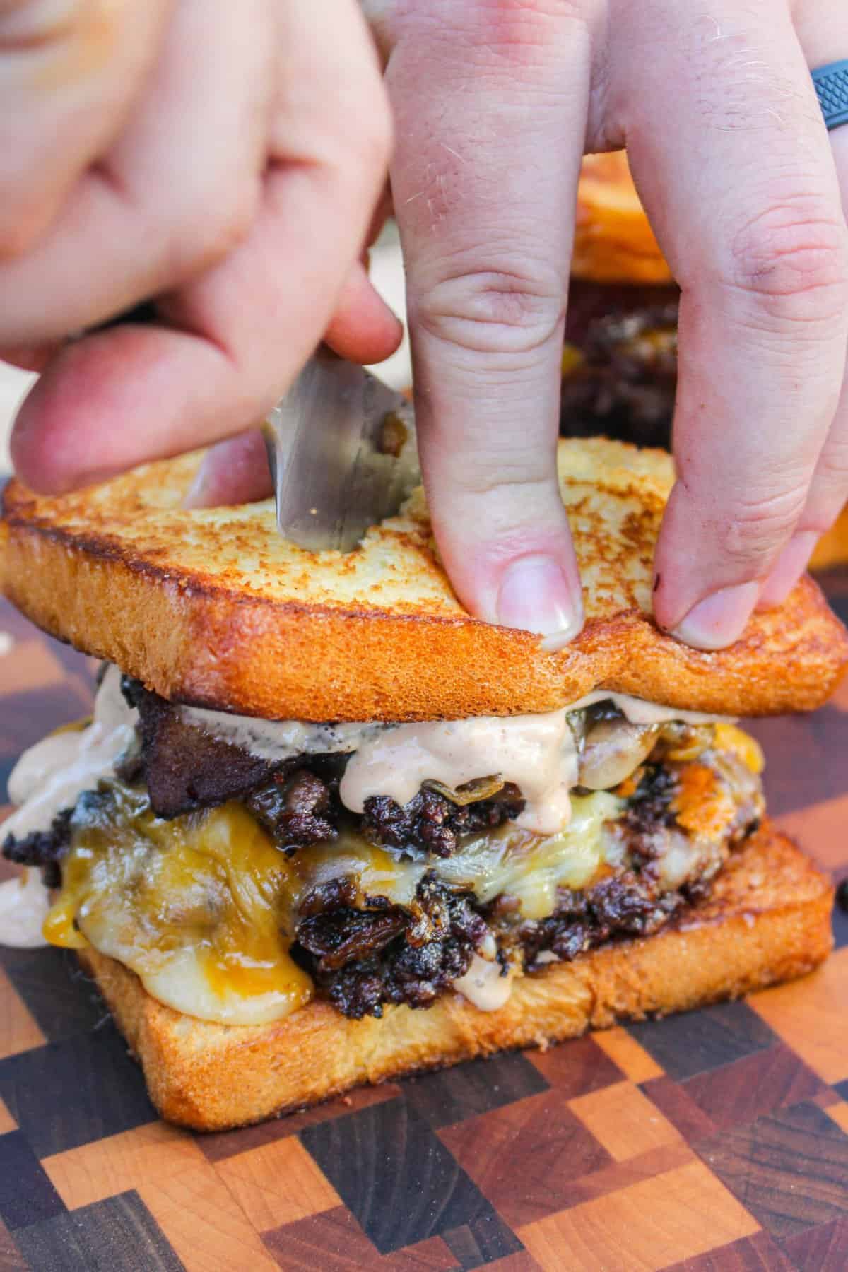 finished cheesy patty melt being sliced and held