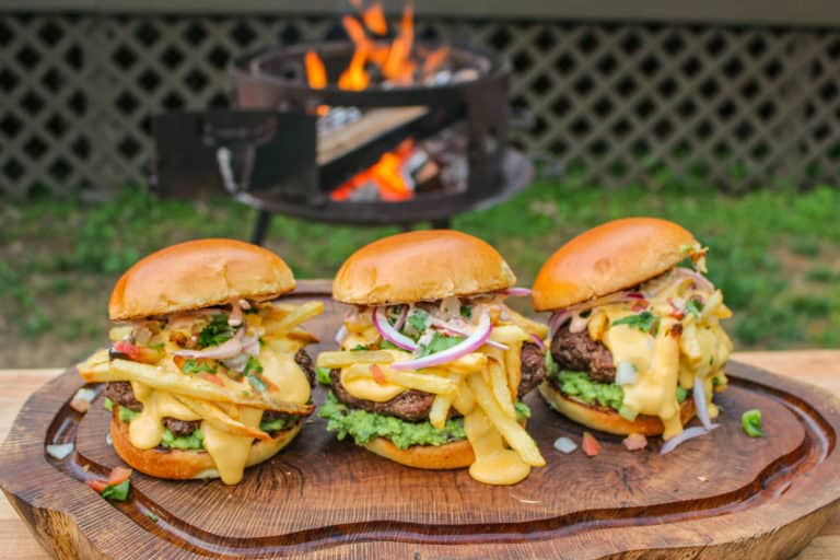 three California Burrito Style Burgers lined up on a cutting board in front of a grill