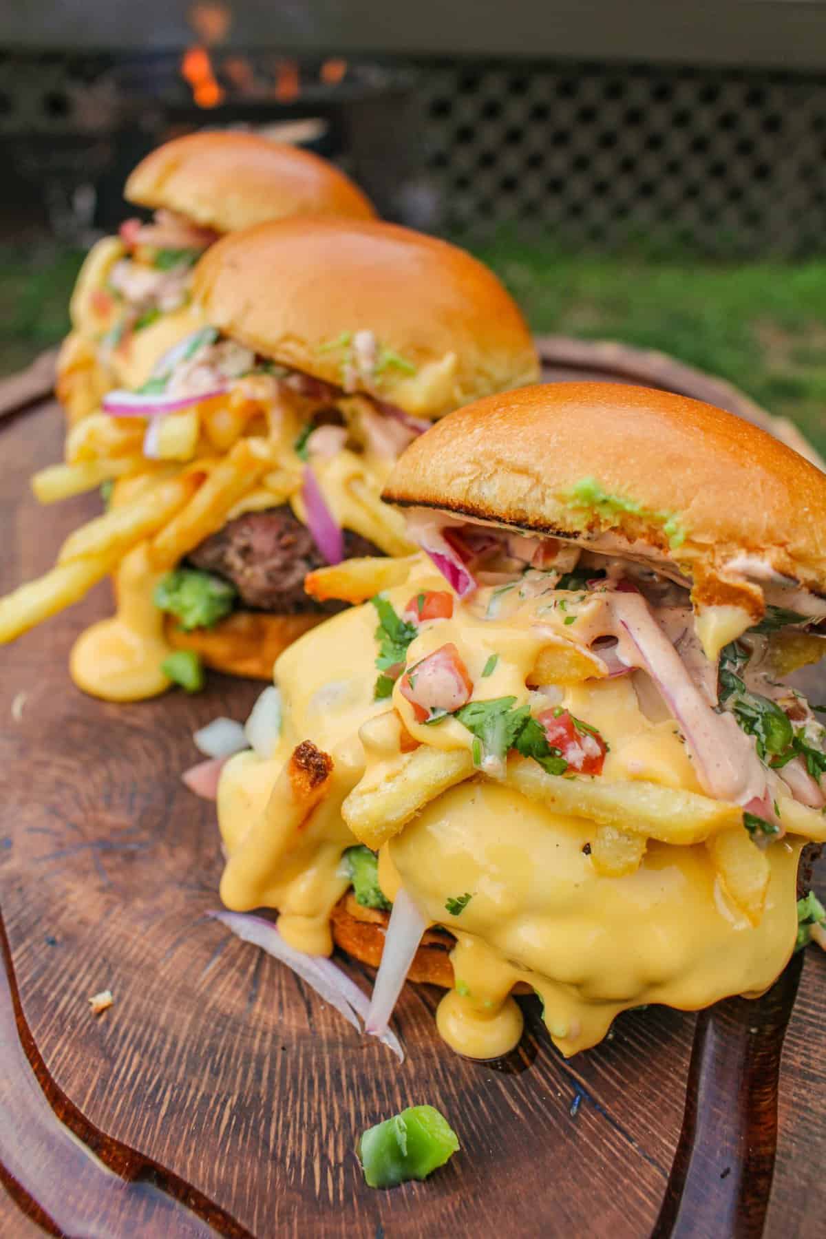 closeup of three loaded burgers lined on a cutting board with one in the forefront