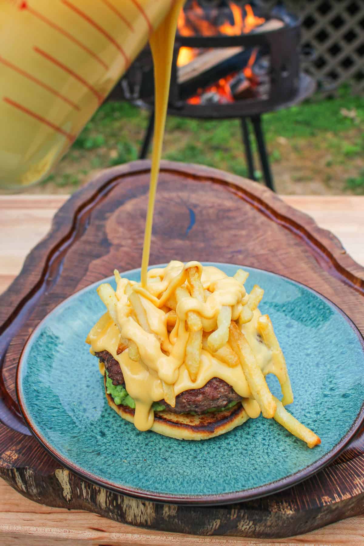 cheese sauce being poured over a burger on a blue plate