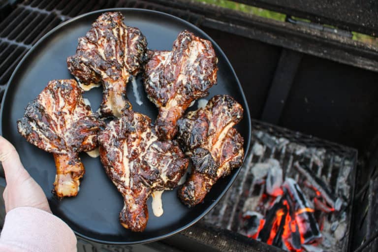 plate of grilled butterflied chicken drumsticks with Alabama white sauce held over the grill