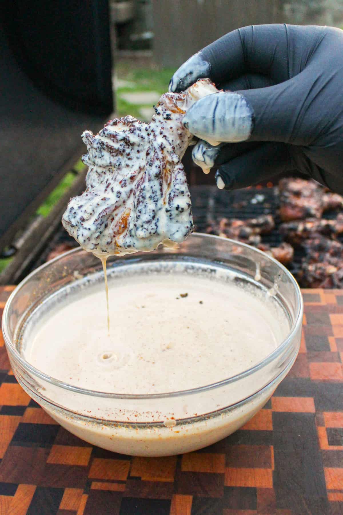 chicken drumstick held over a bowl of Alabama white sauce