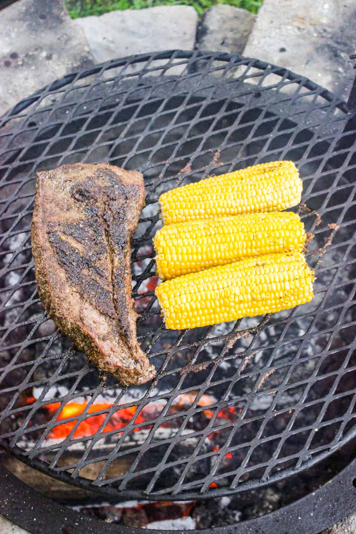 tri-tip on the grill next to three cobs of corn