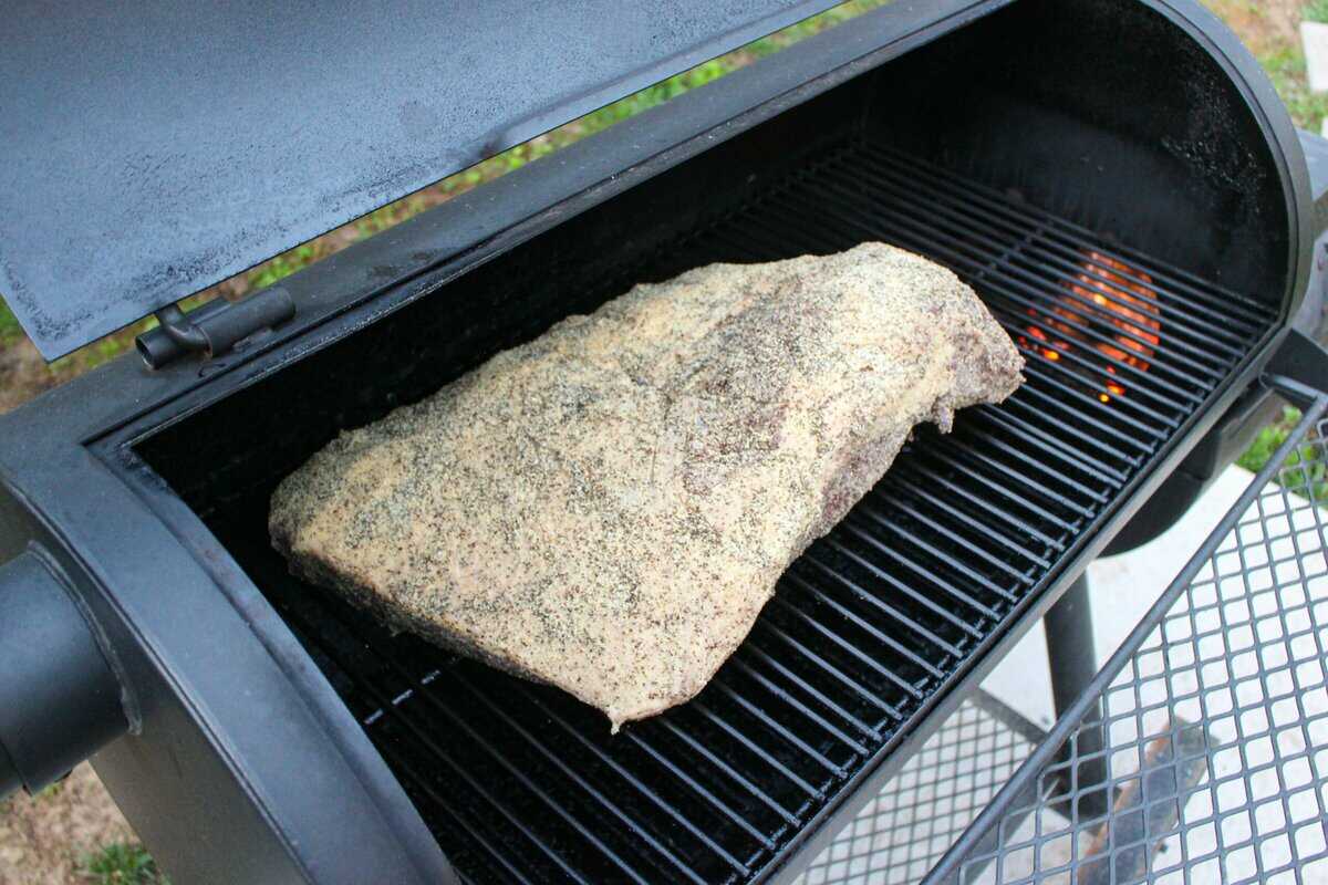 Raw, seasoned brisket getting placed on the smoker. 