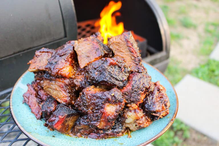 a pile of brisket burnt ends on a plate held next to a smoker