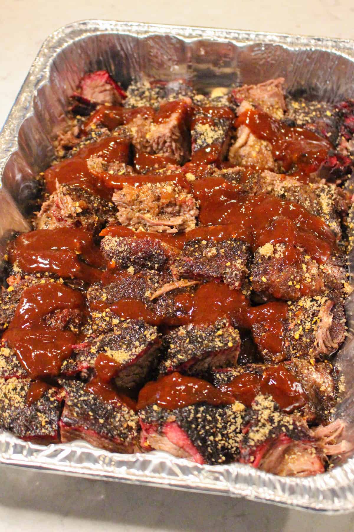 overhead of a foil bin with brisket burnt ends drizzled with sauce