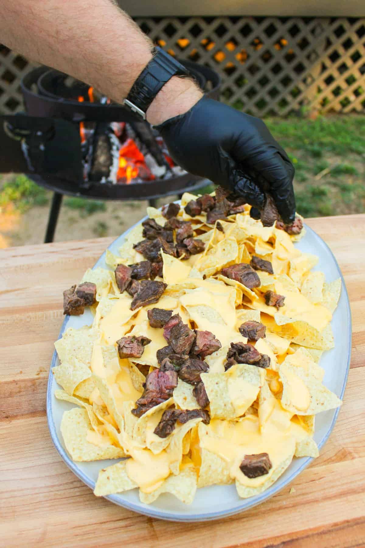 beef being added onto a plate of nachos