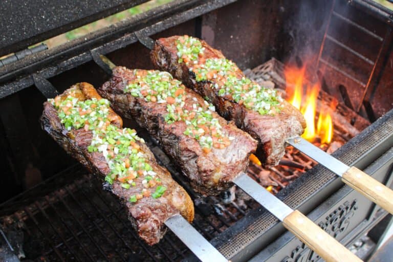 three strip steak skewers topped with salsa vinaigrette over a fire