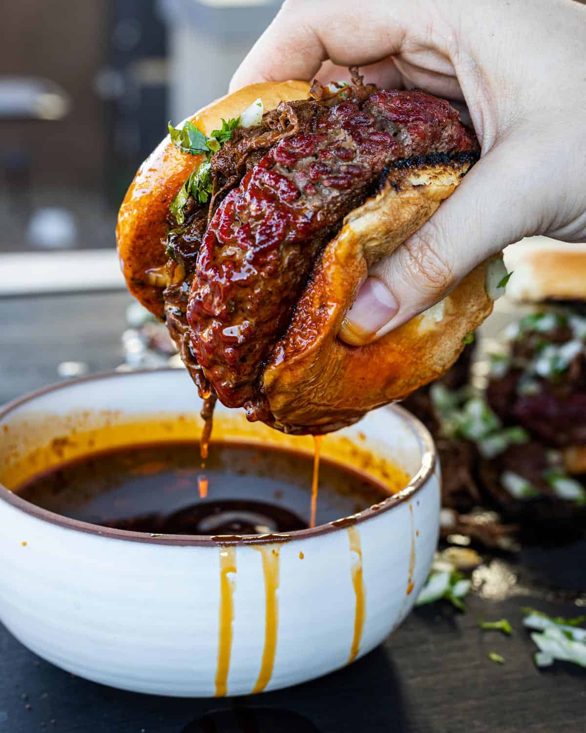 Smoked Birria Burgers getting dipped in the consumme.