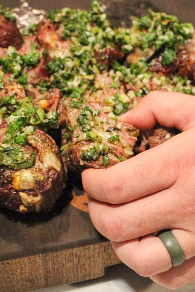 grilled steak pinwheel being lifted off of a cutting board with more pinwheels