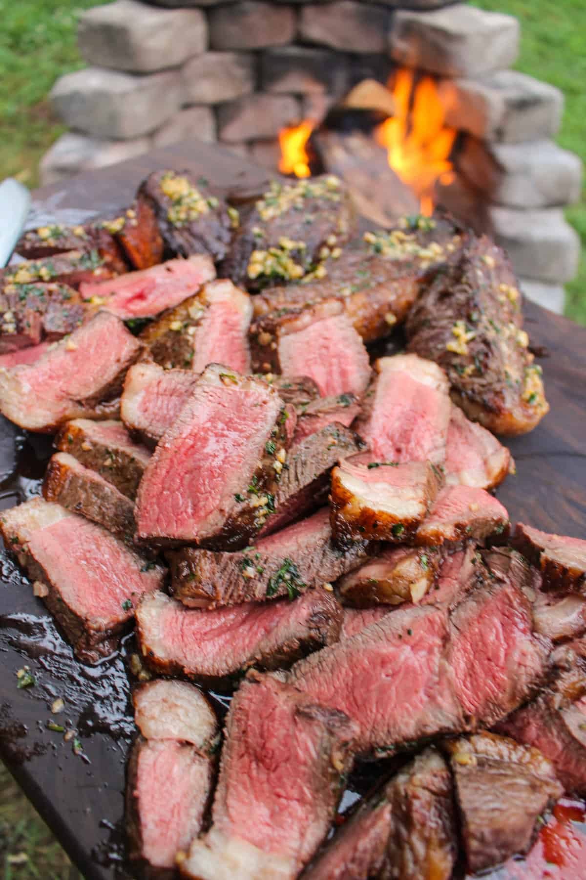 sliced garlic butter picanha on a cutting board held over a fire pit