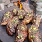 grilled picanha topped with garlic butter held next to a fire pit