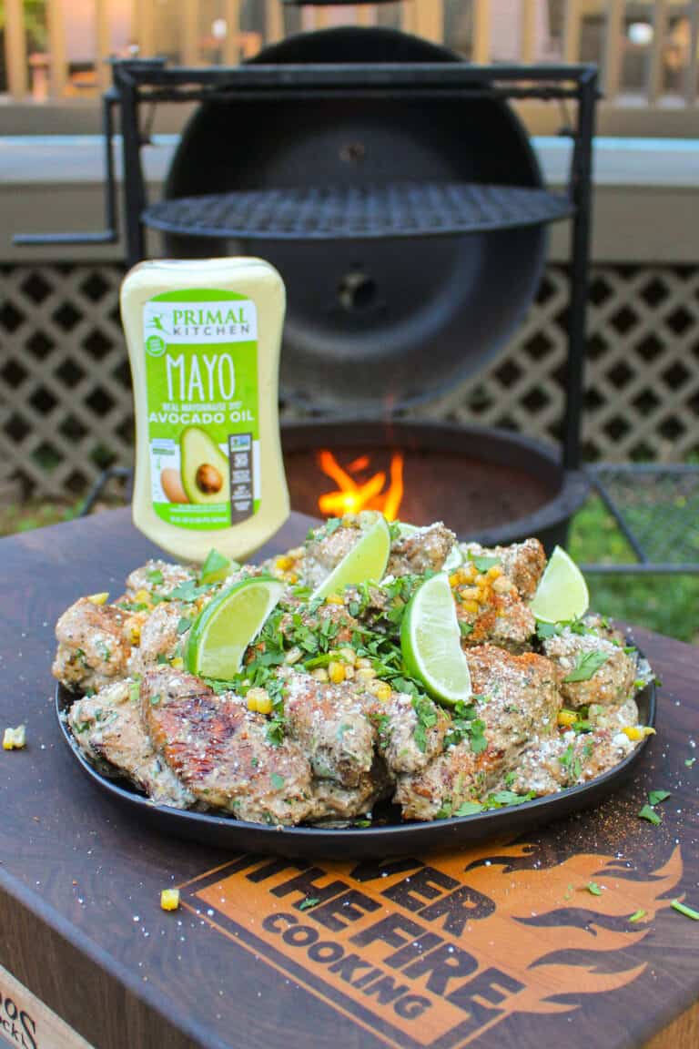 a plate of elote style chicken wings with a bottle of mayo in the background