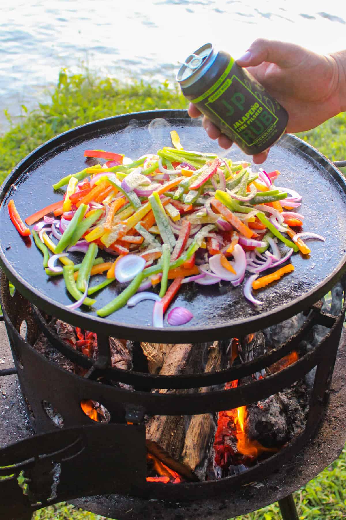 bottle of lime pilsner seasoning held over a plancha full of fajita veggies