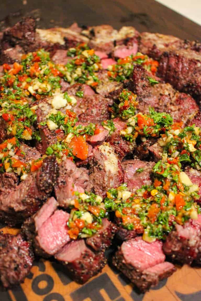 closeup of a pile of cubed steak topped with tomato herb chimichurri