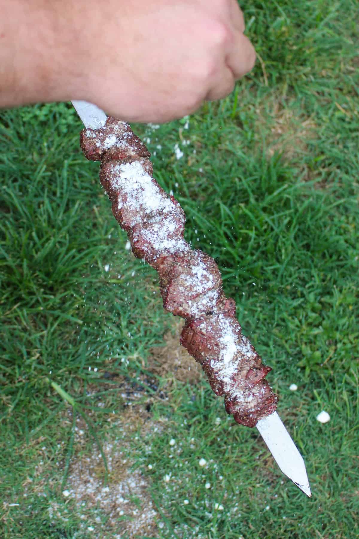 parmesan being sprinkled over a grilled steak skewer