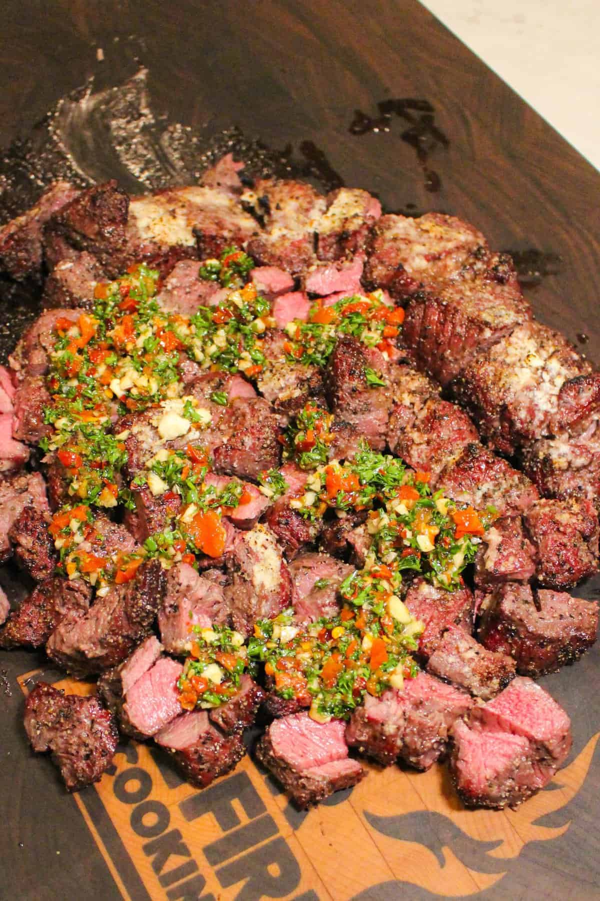 cooked steak topped with chimichurri on a cutting board