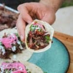 a pulled beef chuck roast taco held over a plate with more tacos