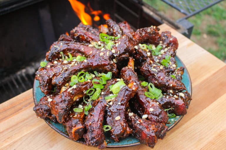 overhead of a plate of peanut butter and jelly sticky ribs next to a smoker