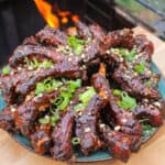 overhead of a plate of peanut butter and jelly sticky ribs next to a smoker