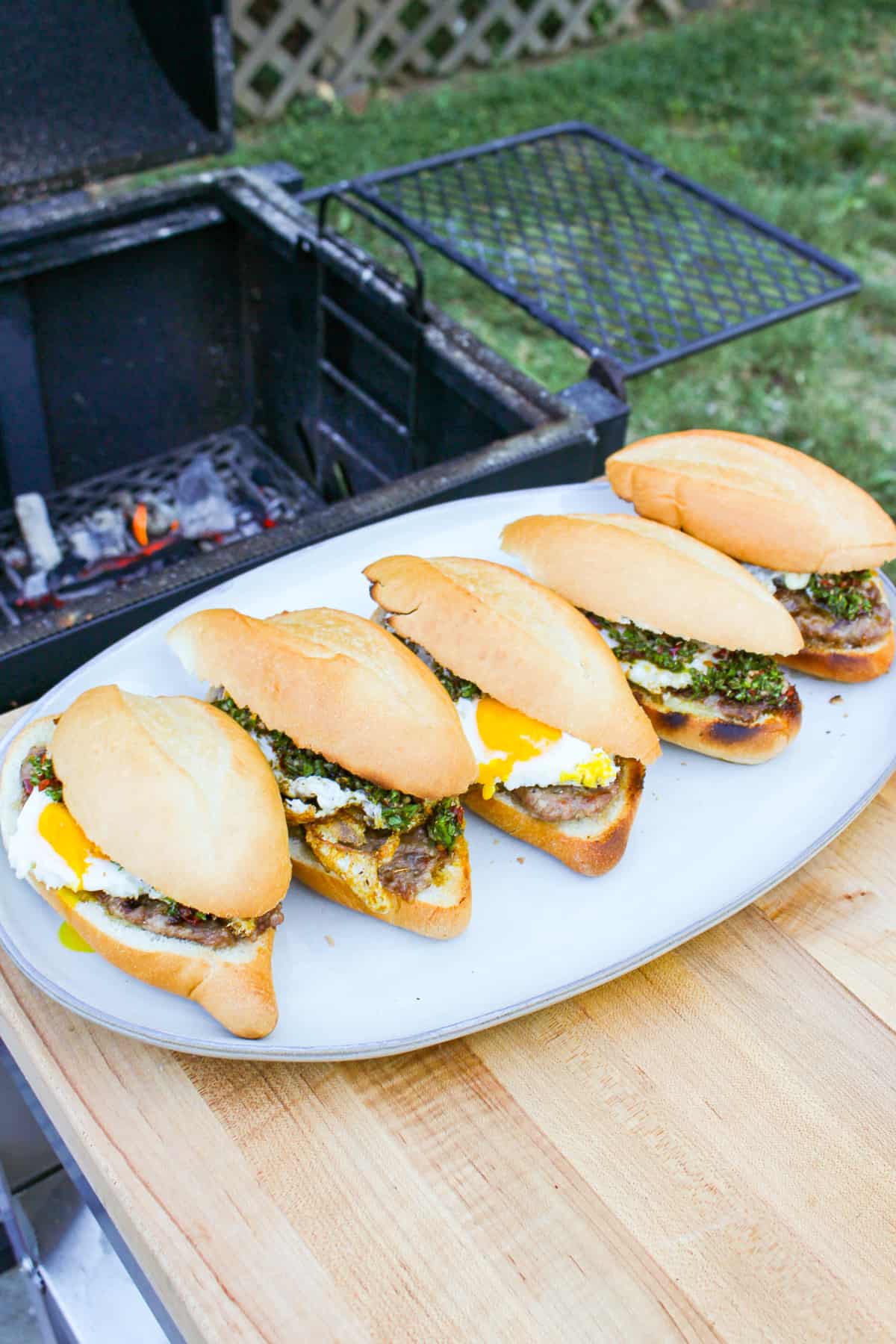 finished cheese stuffed sausage sandwiches on a white platter next to a grill