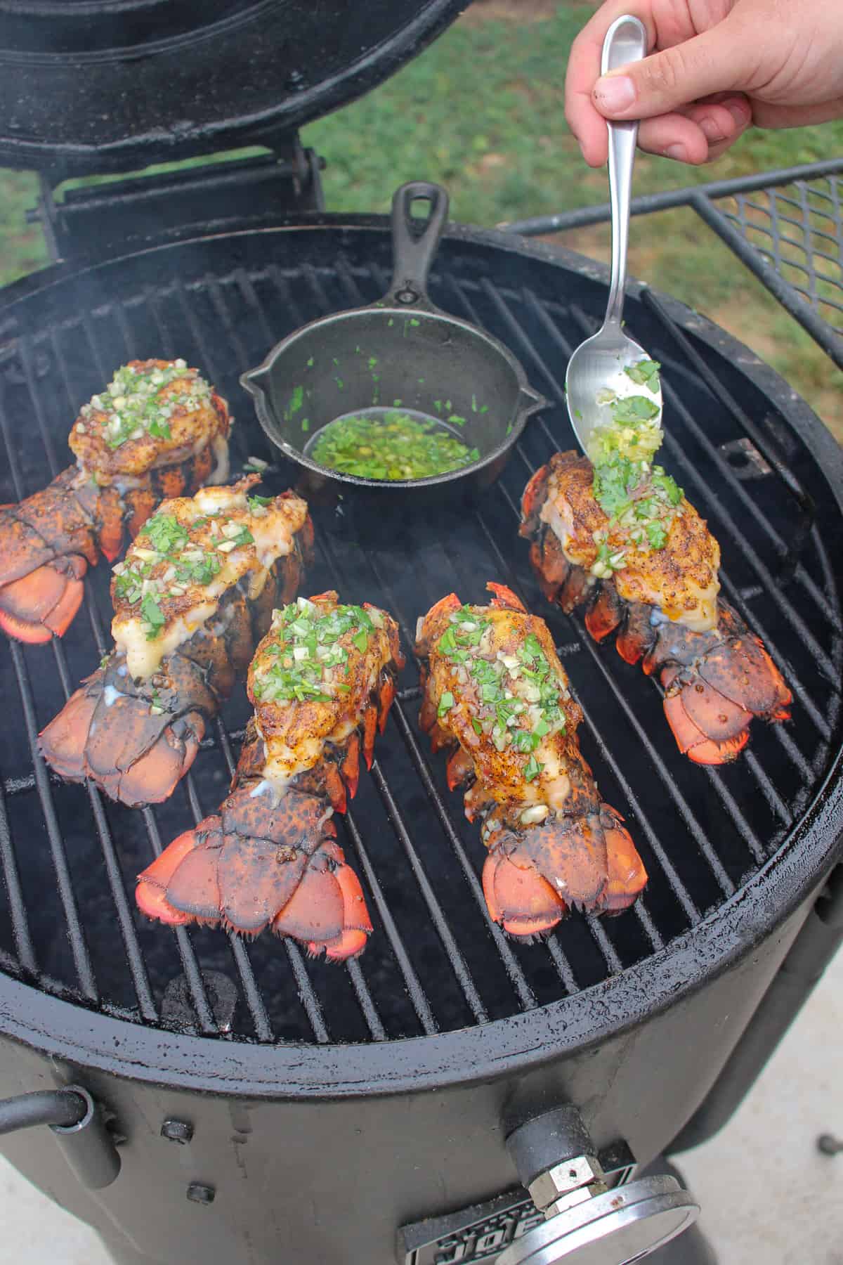 garlic butter being spooned onto smoked lobster on a smoker