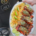 a platter with smoked lobster tails and esquites held next to a smoker