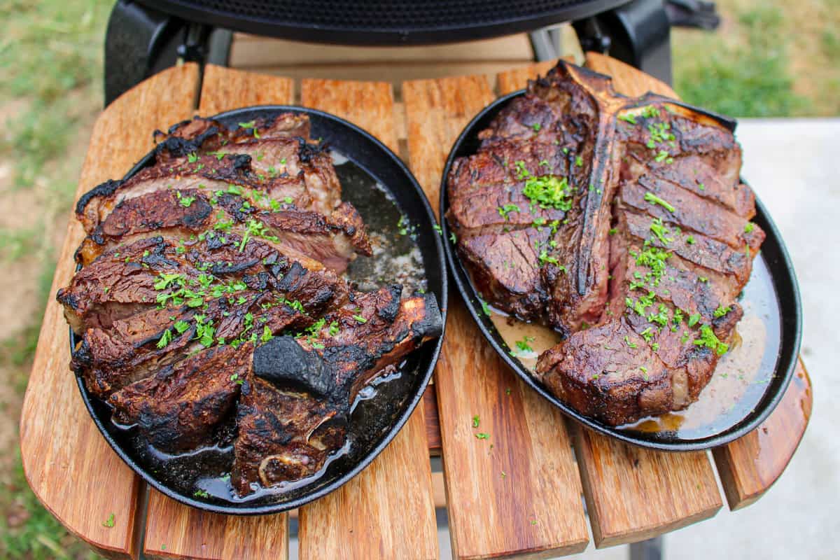 two peter luger style steaks on platters set on a cutting board overhead