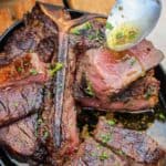 closeup of a plate of steak being drizzled with garlic butter