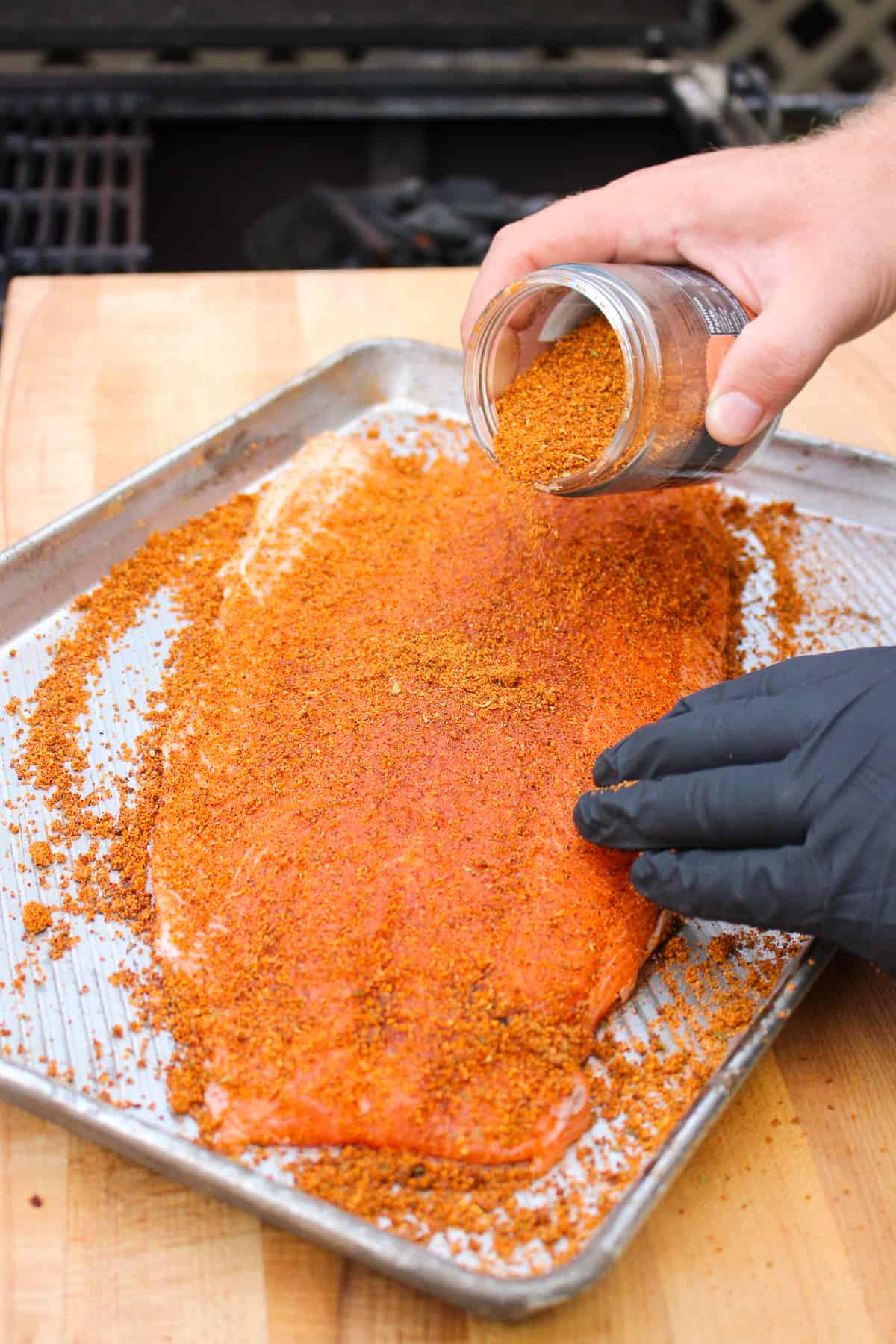 whole salmon on a baking sheet being rubbed with chipotle mezcal seasoning