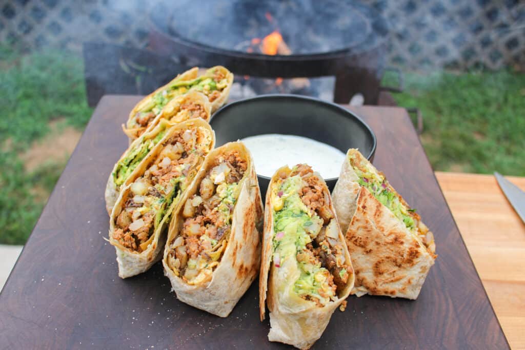 halves of chorizo breakfast burritos lined on a cutting board around a bowl of jalapeño lime sauce